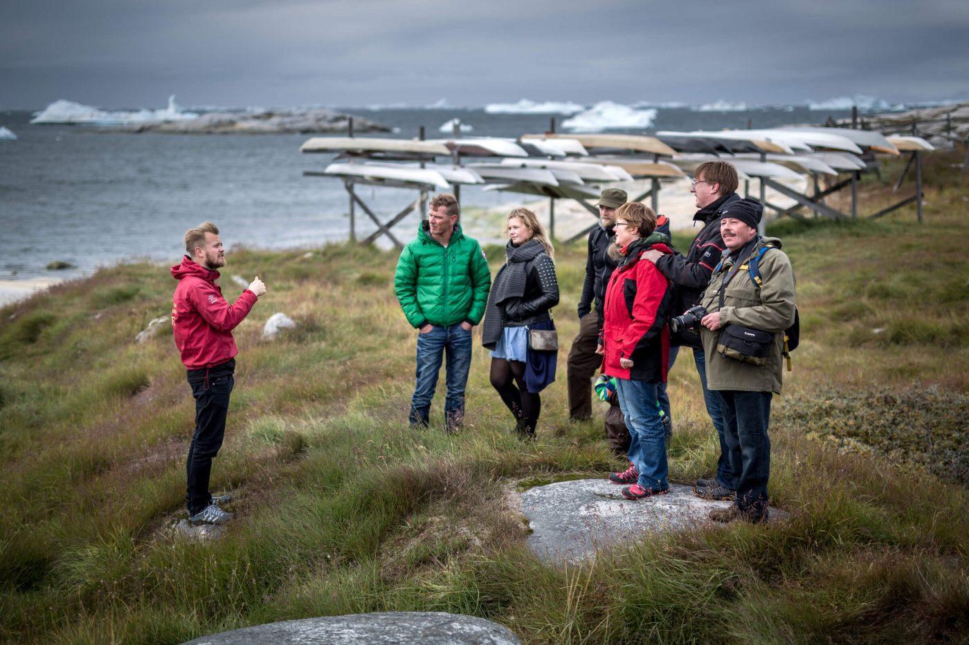 A guided walk in Ilulissat with traditional Greenland kayaks in the background. Photo by Mads Pihl