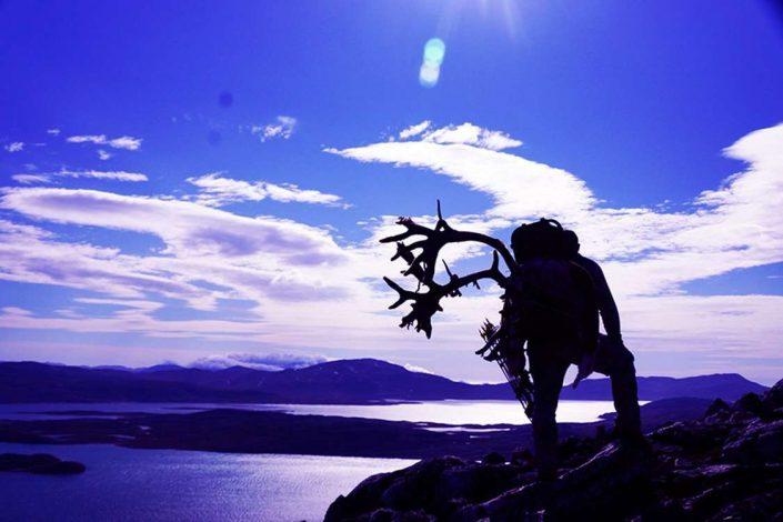 Purple landscape with a silhouette of a man carrying reindeer antlers on his back. Photo by Bowhunting Greenland