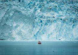 A small passenger boat in front of the huge glacier wall at the Eqi glacier in Greenland. Photo by Mads Pihl