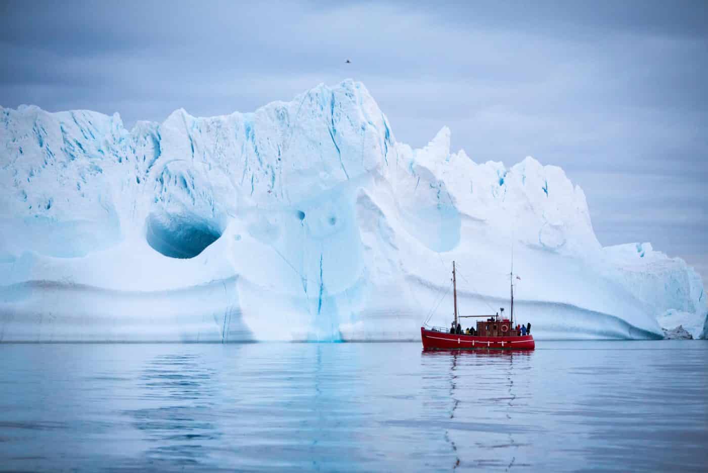 Tourists on a boat tour sailing by a giant iceberg near Ilulissat in North Greenland. By Paul Zizka