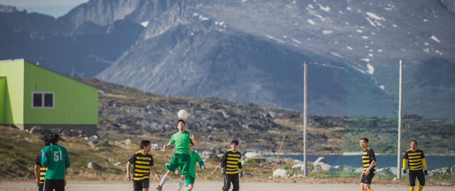 A game of soccer in Nanortalik in South Greenland with a backdrop of rugged peaks. Photo by Mads Pihl, Visit Greenland
