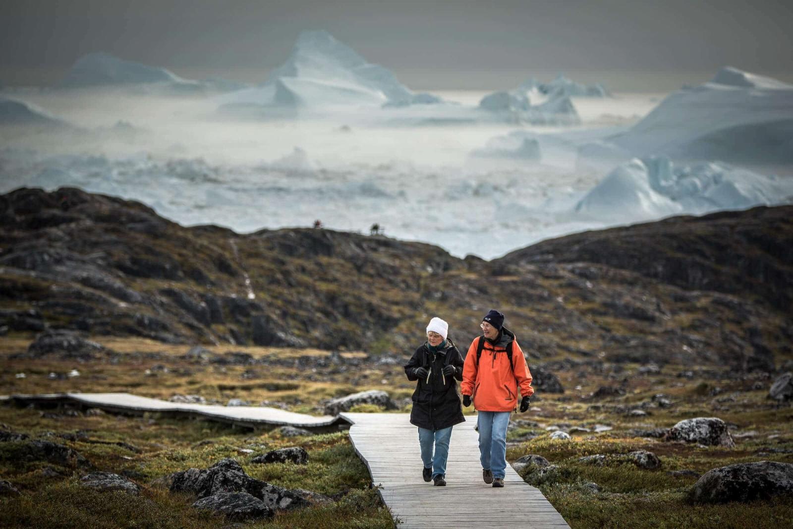 Two women on the boardwalk near Sermermiut with icebergs in the background in Ilulissat in Greenland