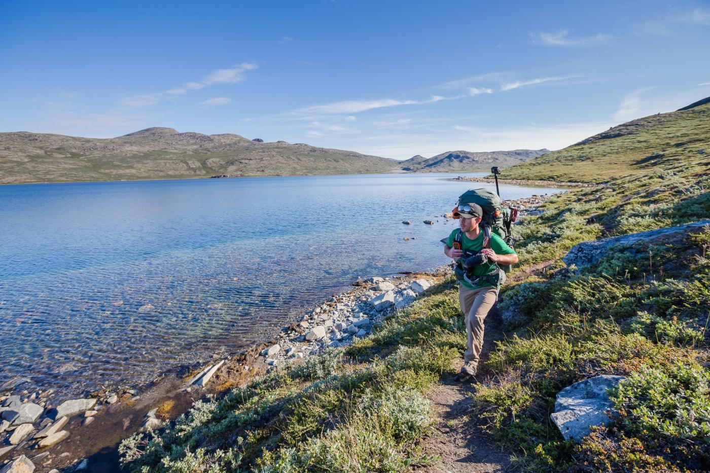 Male hiker walking on a path next to a lake on the Arctic Circle Trail.