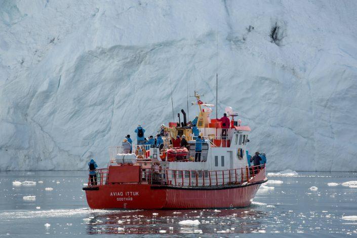 A tour boat in fron of an iceberg wall in the Ilulissat Icefjord in Greenland