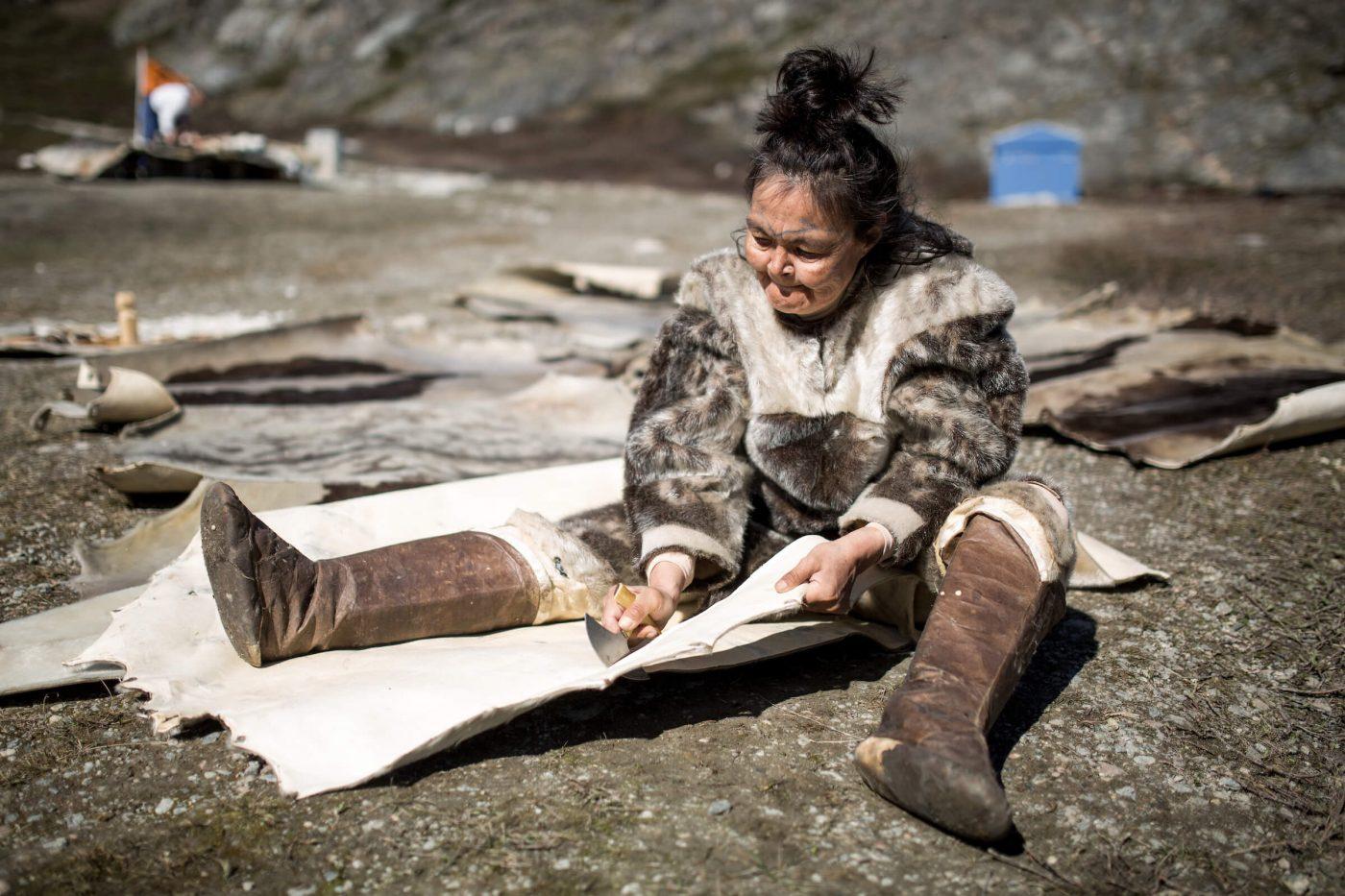 A woman carving seal skin for a tent at the living village museum in Qasigiannguit in Greenland, by Mads Pihl