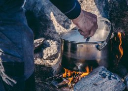 Guide cooking backcountry dinner over an open fire near the Arctic Circle. By Raven Eye Photography