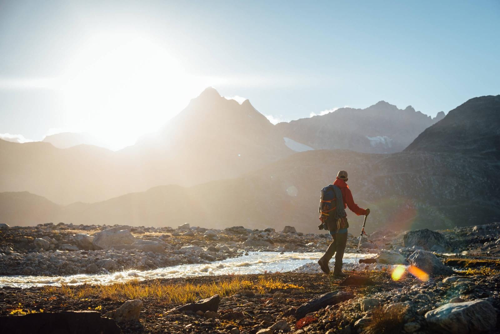 Hiker looking at the mountains during sunset near river, Near Camp In Tasiilaq Fjord. By Chris Brinlee Jr