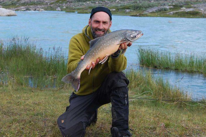 CEO Thomas Olsen of North Safari Outfitters standing with an Arctic char. Photo by North Safari Outfitters