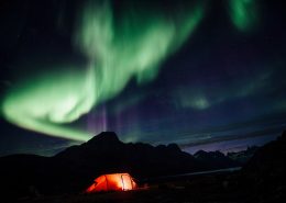 Northern lights over a lit tent, Camp In Tasiilaq Fjord. Photo by Chris Brinlee J