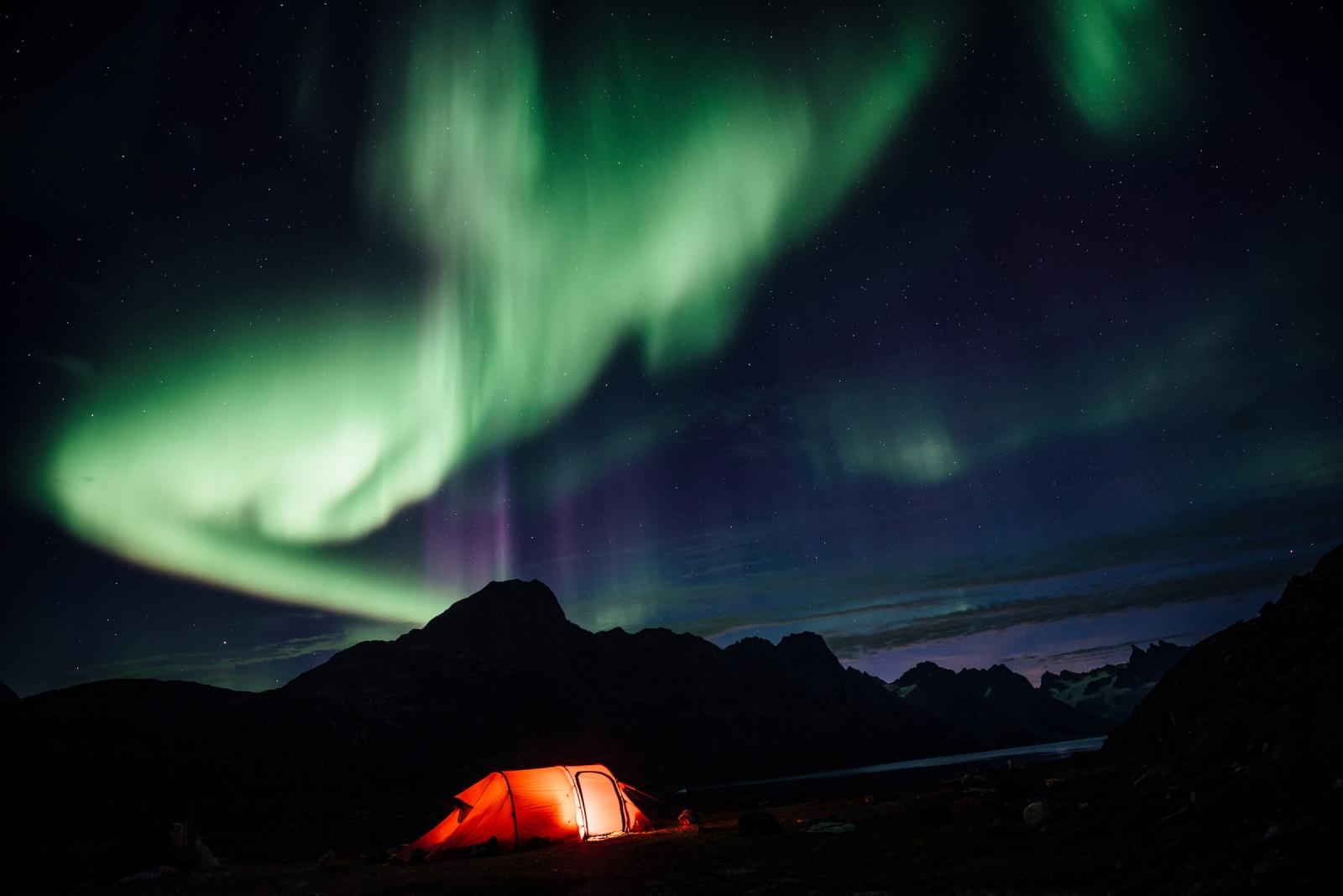 Northern lights over a lit tent, Camp In Tasiilaq Fjord. By Chris Brinlee Jr