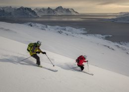 Two skiers in the sunset descending towards the fjord near Kuummiut in East Greenland. By Mads Pihl