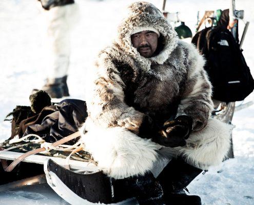 Man sitting on a sled in North Greenland. By André Shoenherr