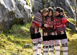 Three girls with a smartphone in greenlandic traditional clothes. By David Trood