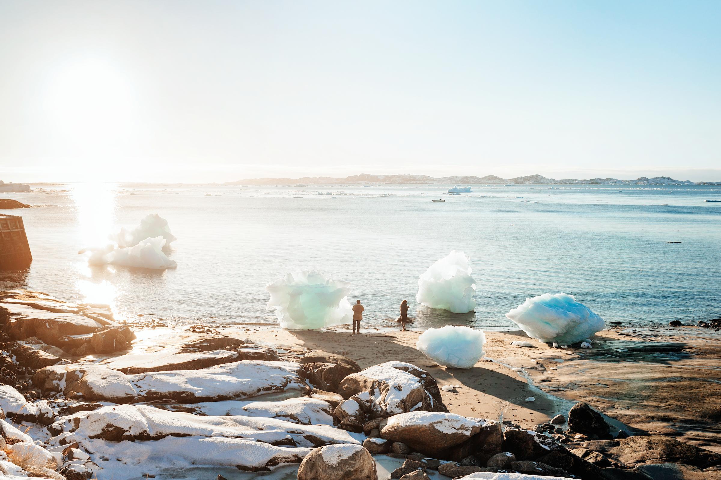 Two tourists on the beach in the colonial harbour of Nuuk in Greenland taking photos of washed up iceblocks in the sunset. Photo by Rebecca Gustafsson