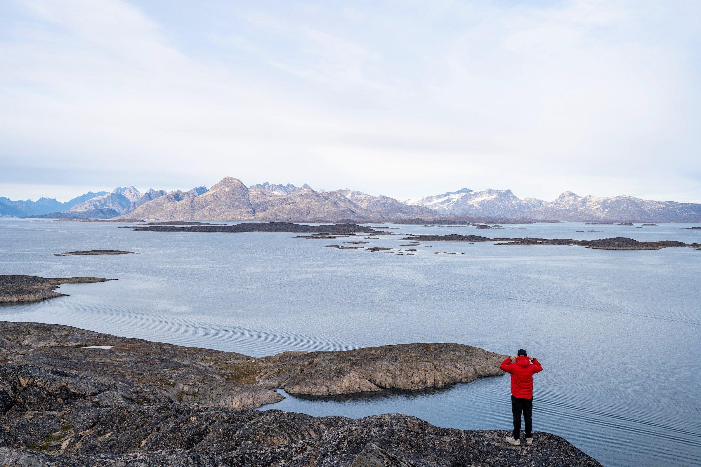 A tourist in red jacket looking over fjord of Maniitsoq from top of a mountain. Photo by Filip Gielda - Visit Greenland