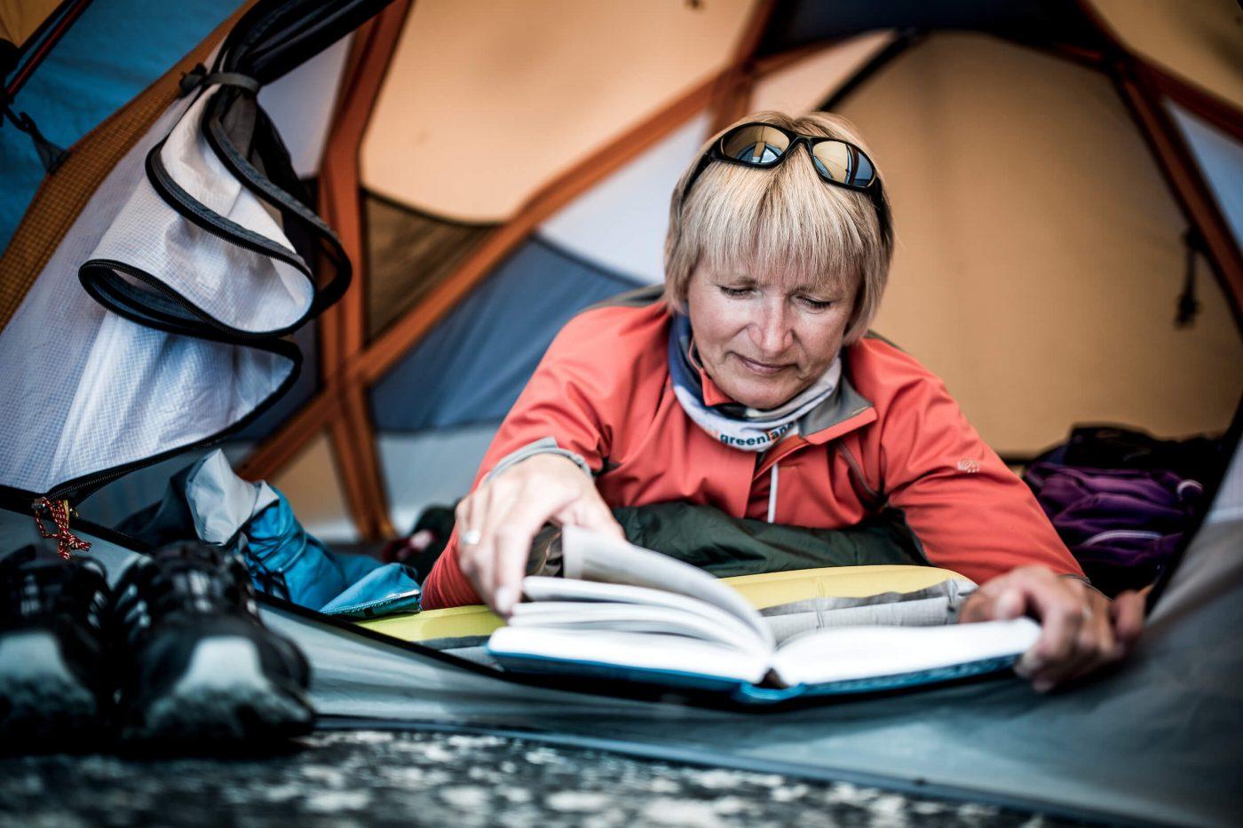 A hiker reading a book in a tent in East Greenland. By Mads Pihl
