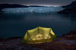 A lamp lit tent near the Eqi Glacier at dusk in Greenland. Photo by Mads Pihl