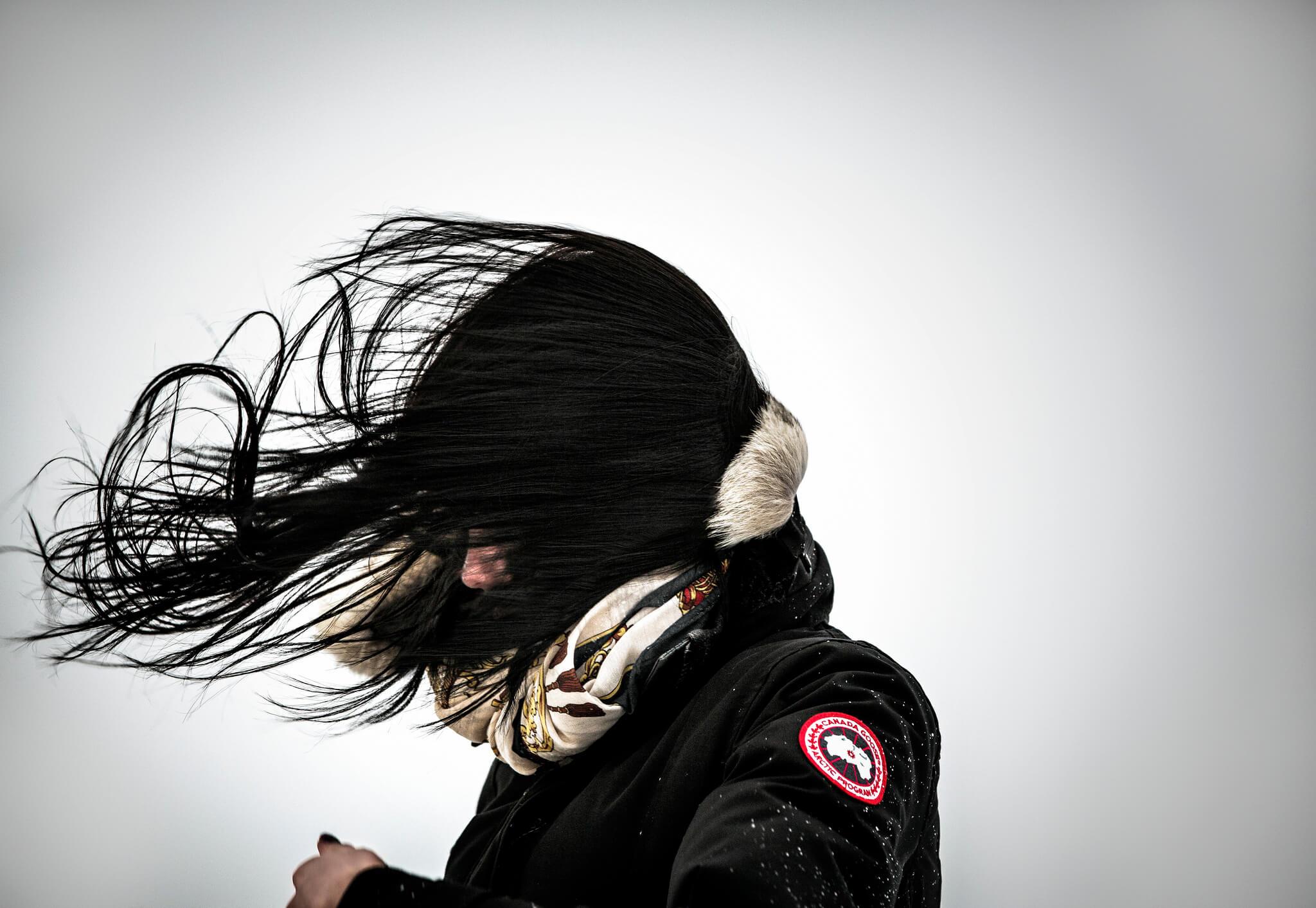 Woman with hair blowing in strong wind in Greenland, by Mads Pihl